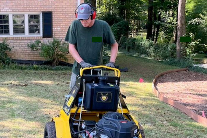 A landscaper aerating a lawn with a yellow aerator. Aeration