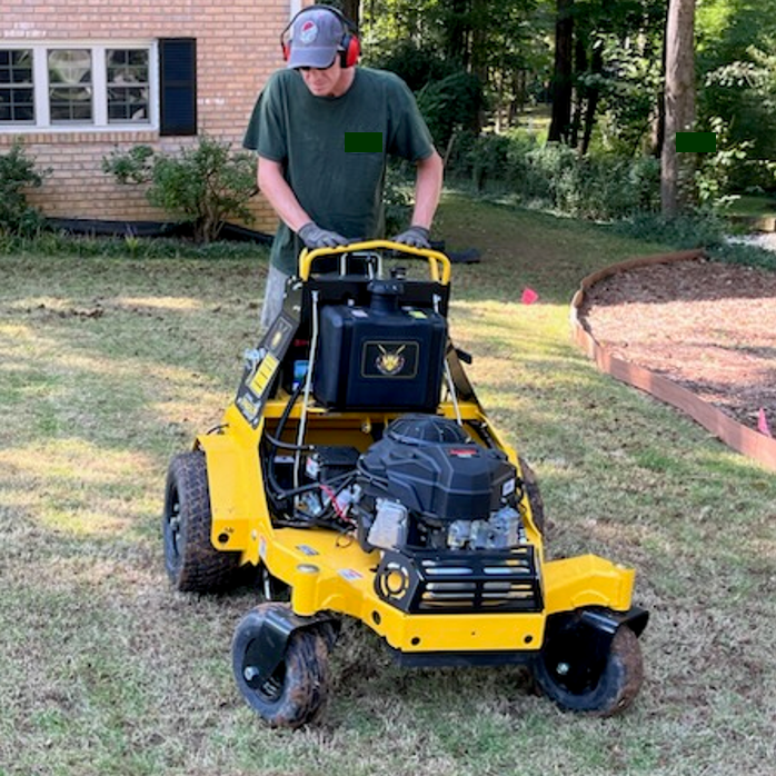 A landscaper aerating a lawn with a yellow aerator. Aeration